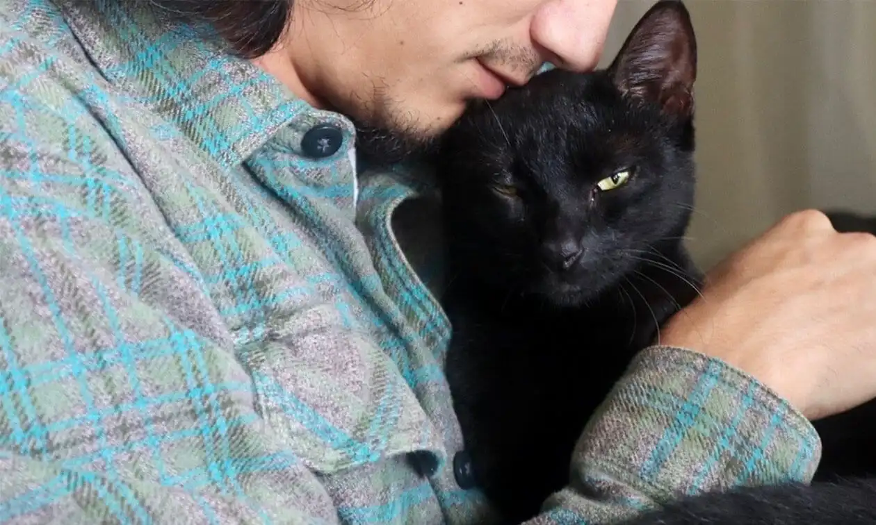 A man holding a black cat in his arms.