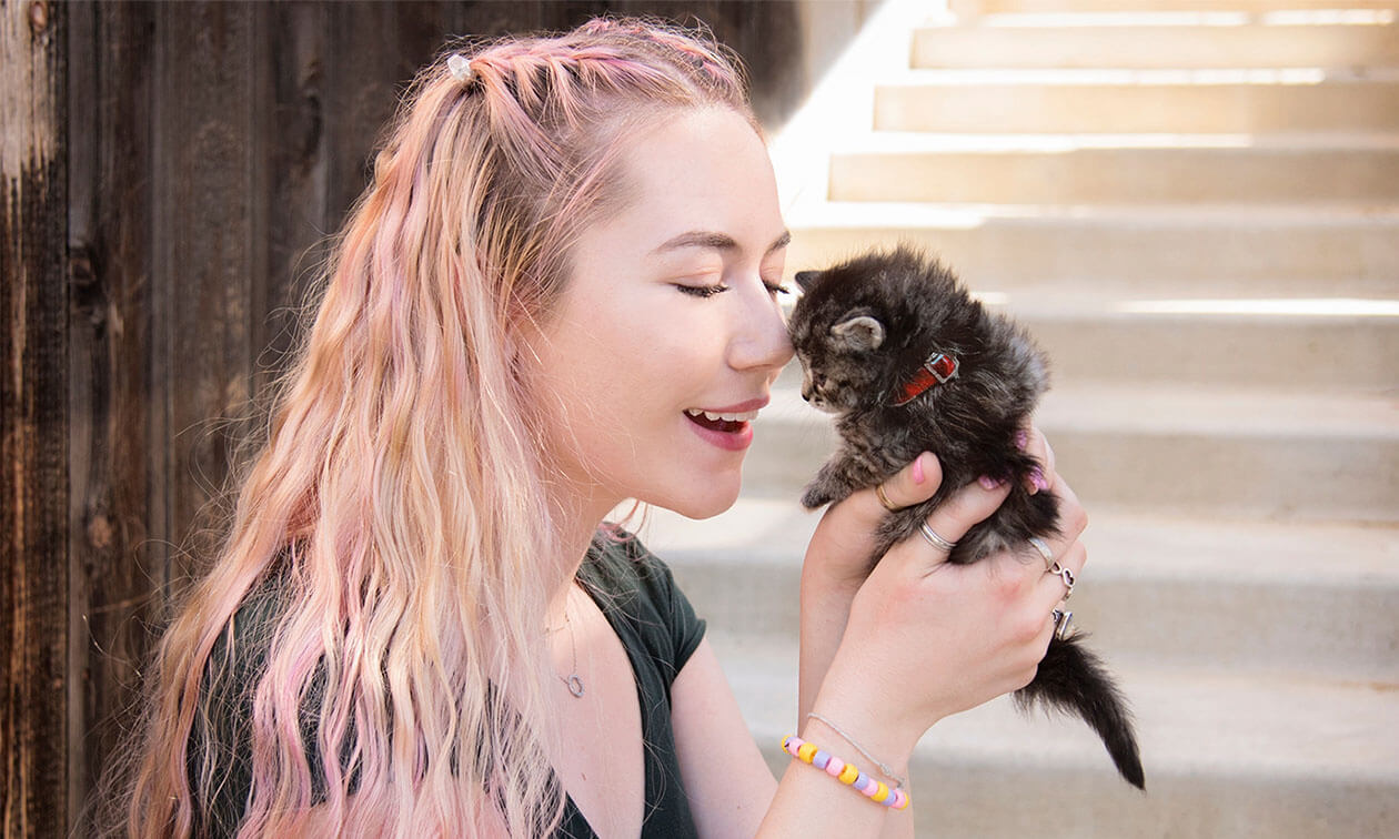 A woman holding a small kitten in her hands.