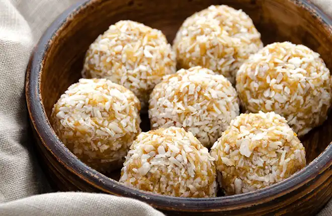 A wooden bowl filled with coconut balls on top of a table.