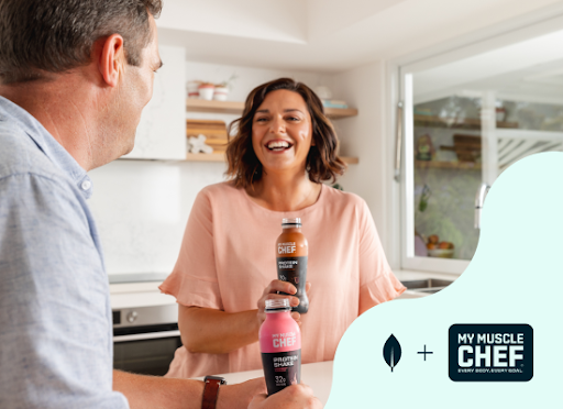 A man and woman smiling together while holding a protein shake bottle, capturing a joyful shared moment.