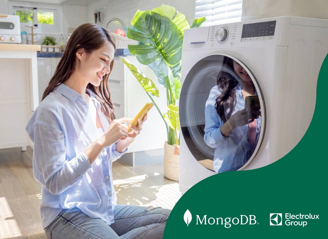Young woman sitting near a washing machine, looking at her smartphone and smiling.