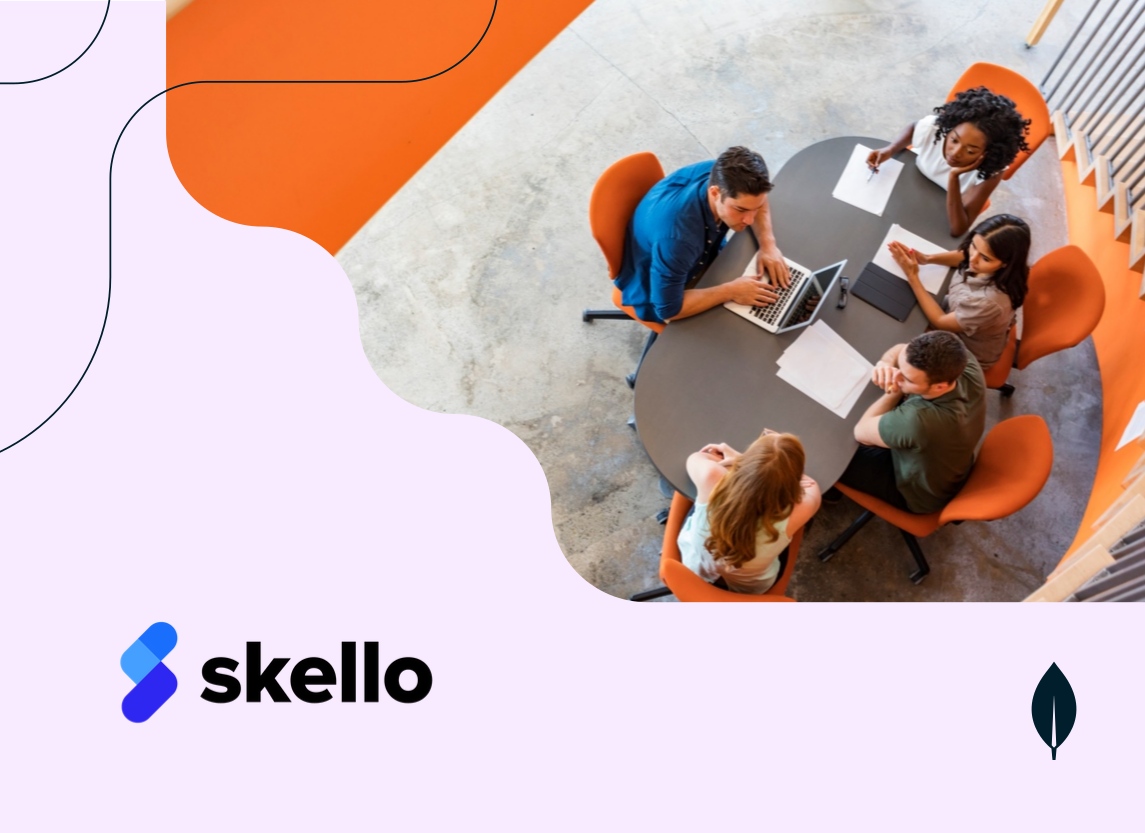 A group of people seated around a table with a laptop and papers, engaged in a discussion.