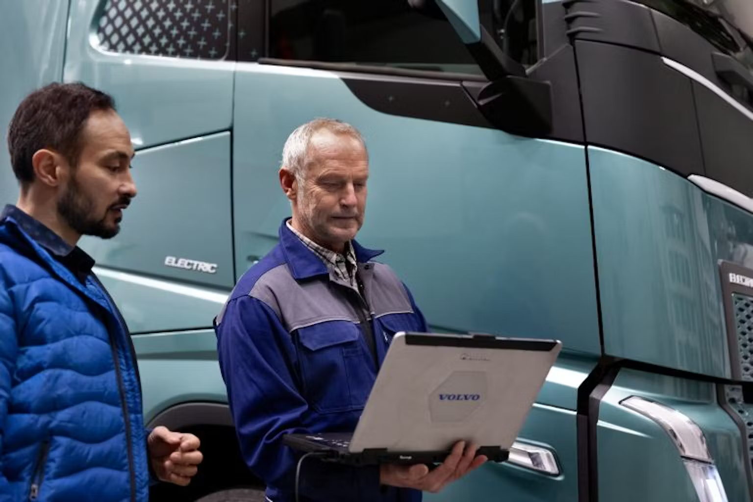 Two employees of Volvo working on a laptop together next to a truck