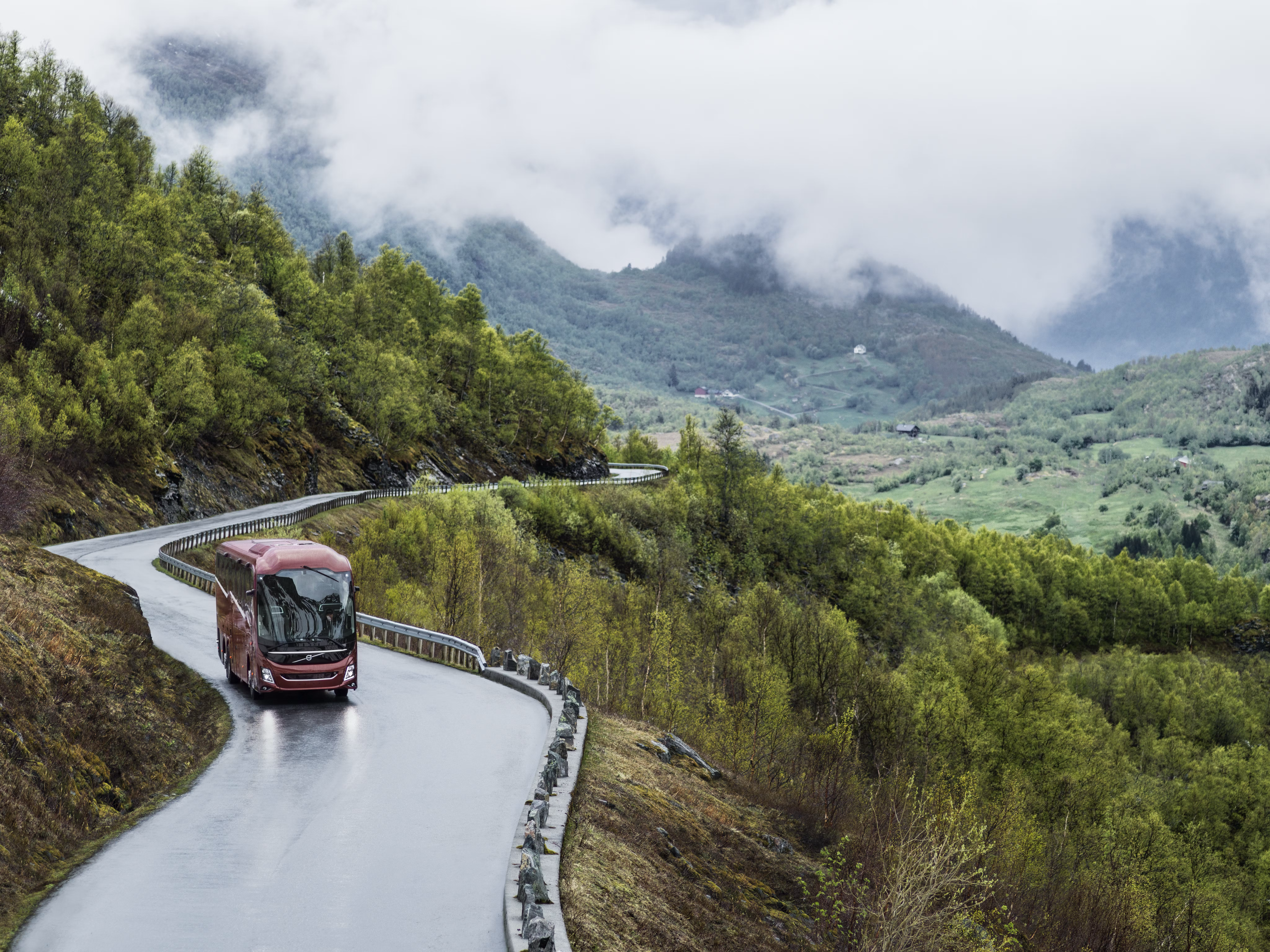 A Volvo bus driving on a road overlooking a countryside.