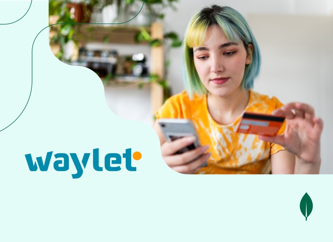 A young woman looking at her phone while holding a payment card in her other hand.