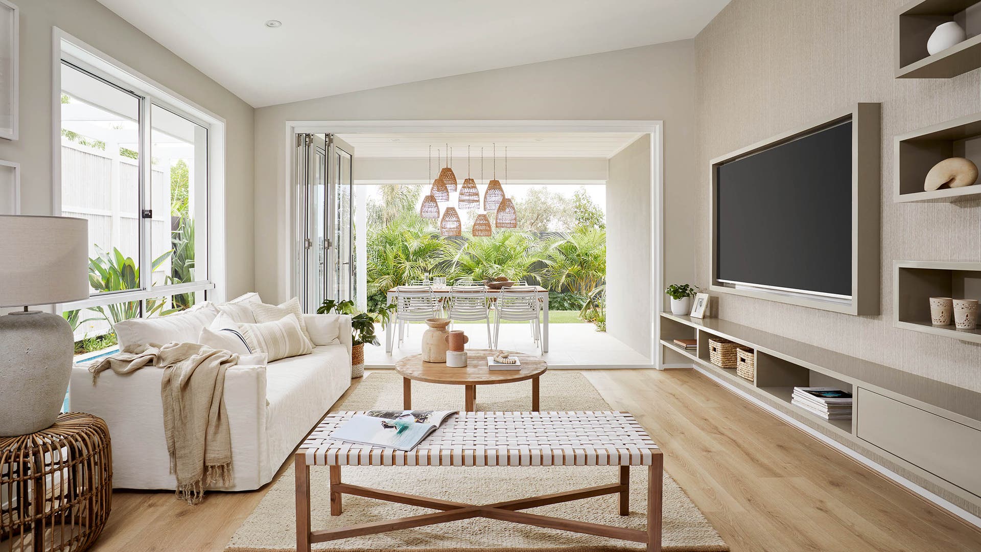 Living room area with a tropical vibe chandelier, warm neutral-toned walls, and a large open glass door entrance.