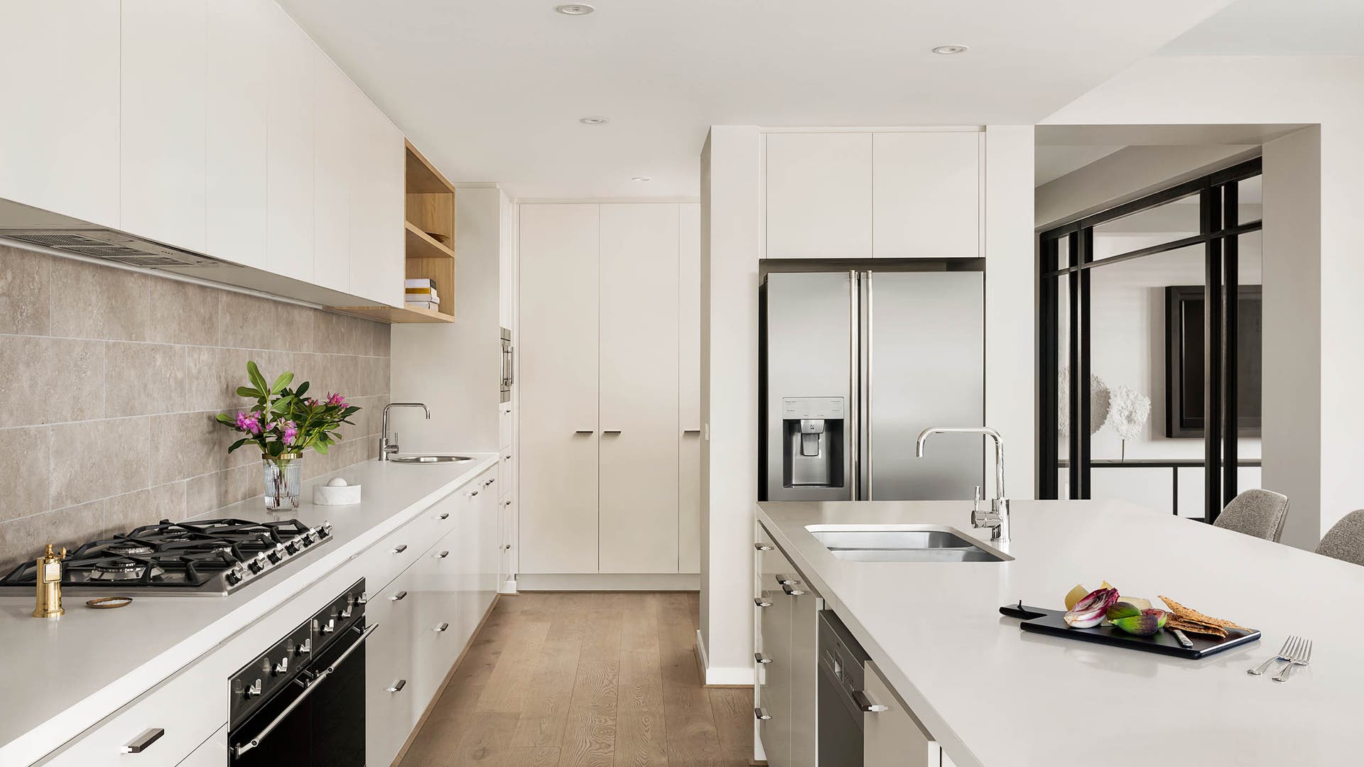 Open plan kitchen with crisp whites with a light grey feature tiled splashback, light wood open cabinetry and light oak wood flooring.