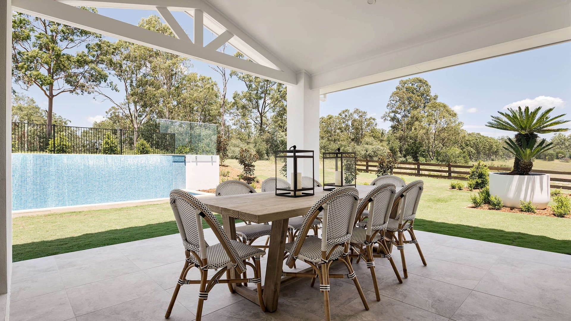 Alfresco area with a timber dining table and stylish chairs, surrounded by a green field.