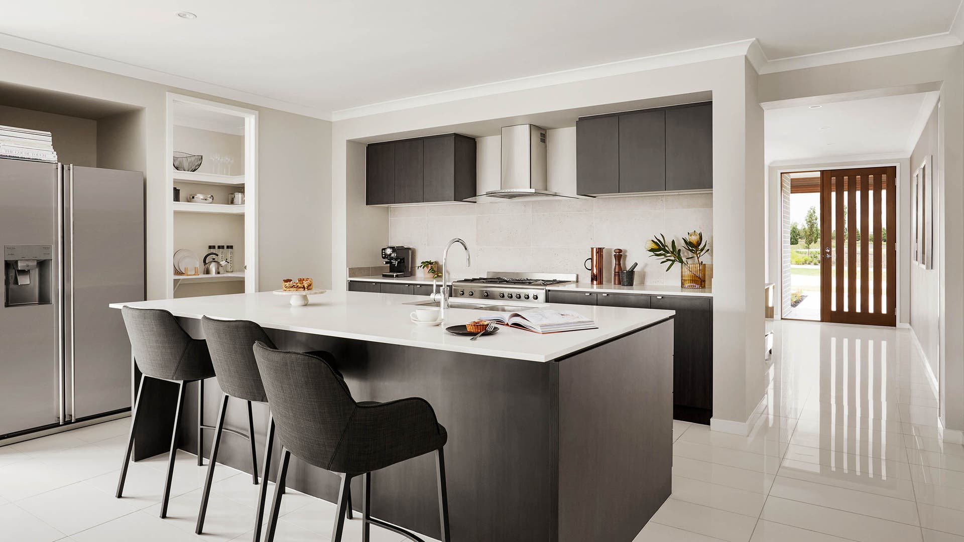 Open kitchen featuring exposed rangehood, tiled spashback, dark grey cabinetry and white benchtops plus tiled flooring.