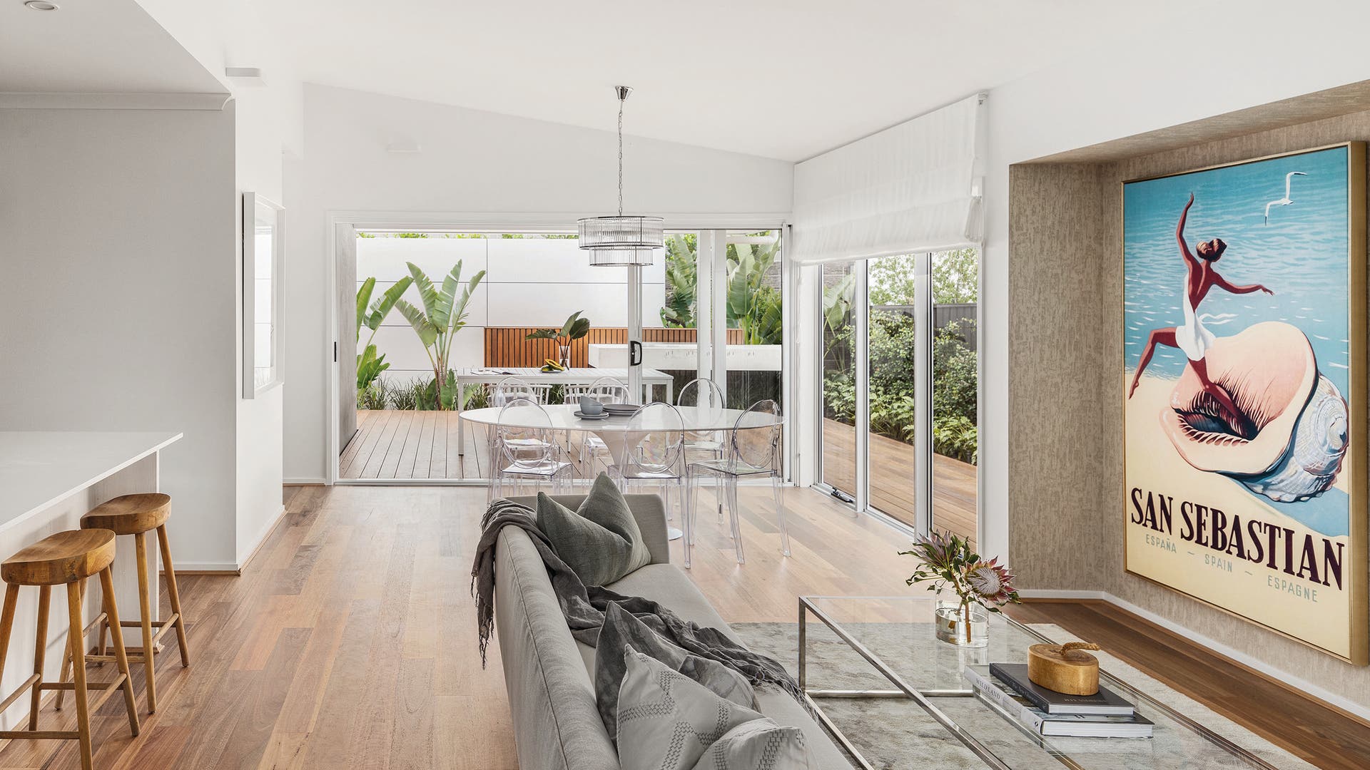 Spacious dining and living area with large open windows, botanical beach-themed interior, and wooden flooring.