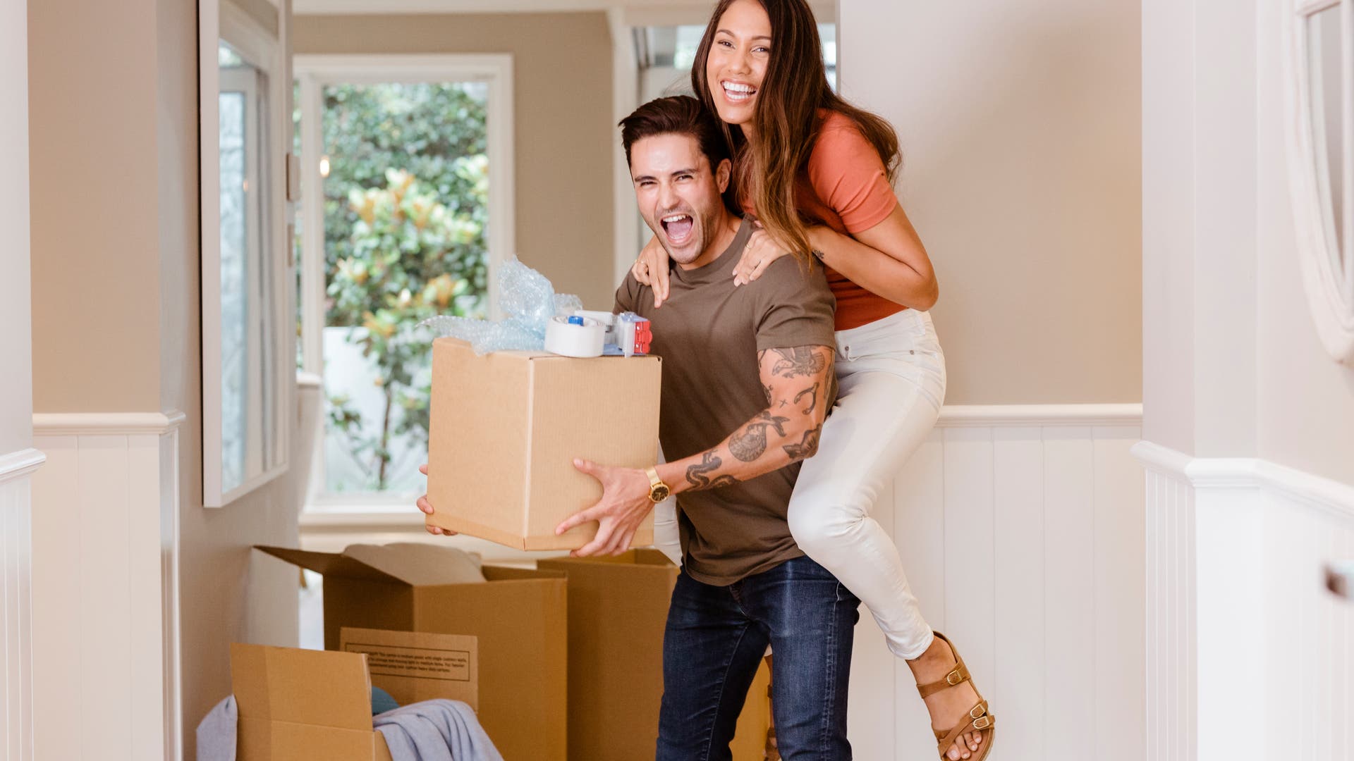 Smiling couple happily moving into their new home, surrounded by unpacked boxes.