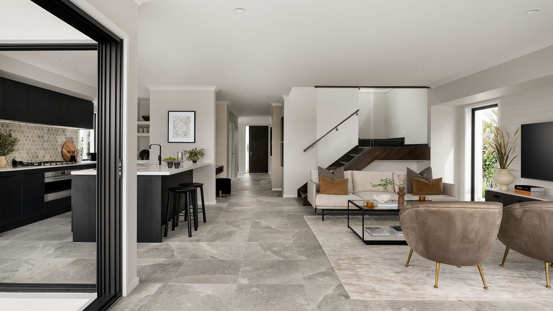 Grey and neutral warm-toned kitchen and living room with dark wooden stairs to the second floor.