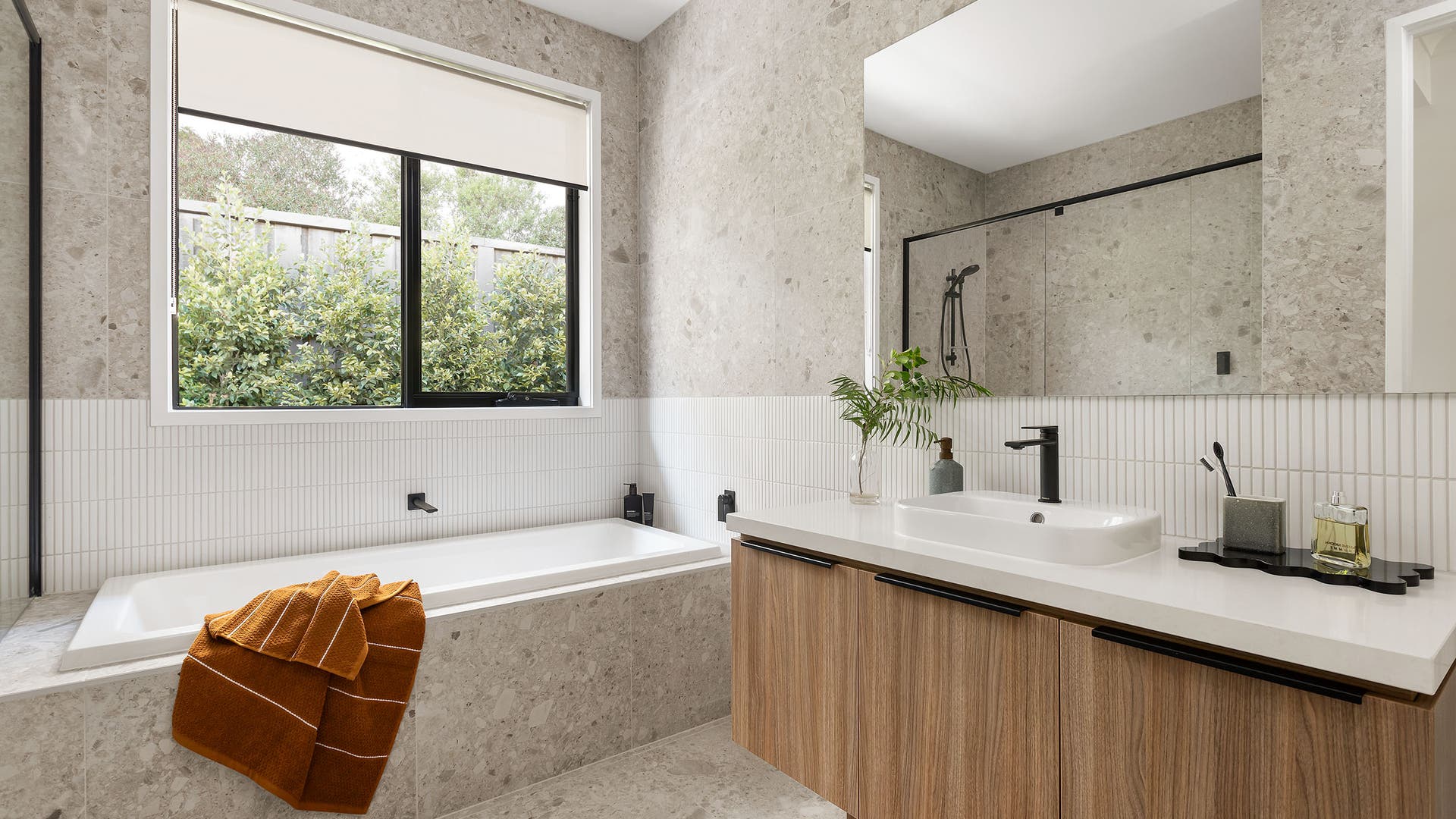 Bathroom featuring striking white kitkat tiles, terrazzo tiles to the walls and floor, black window frames and wood look cabinetry.