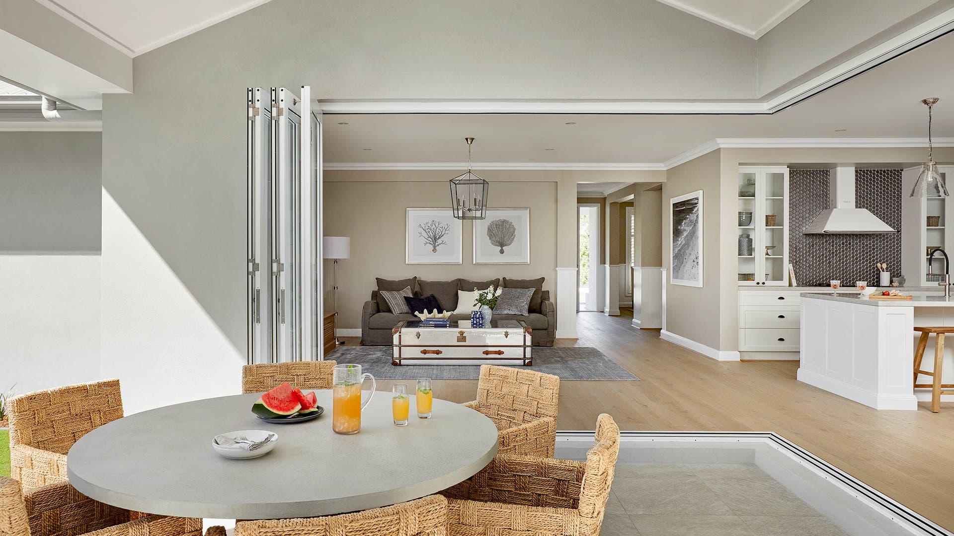 Modern living and alfresco area with warm, neutral-toned walls, timber flooring, and a chandelier.