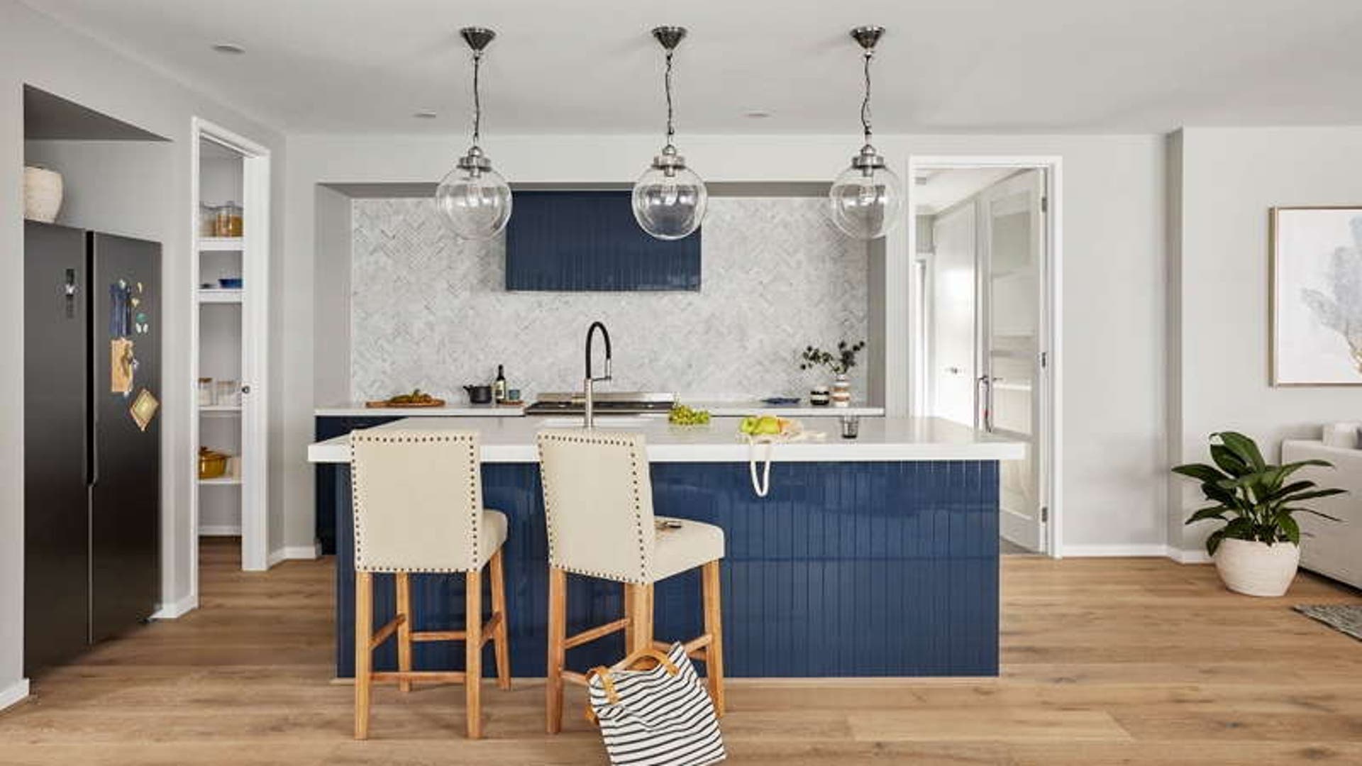 Modern kitchen with timber flooring, deep blue tile cabinets, and pendant lights.