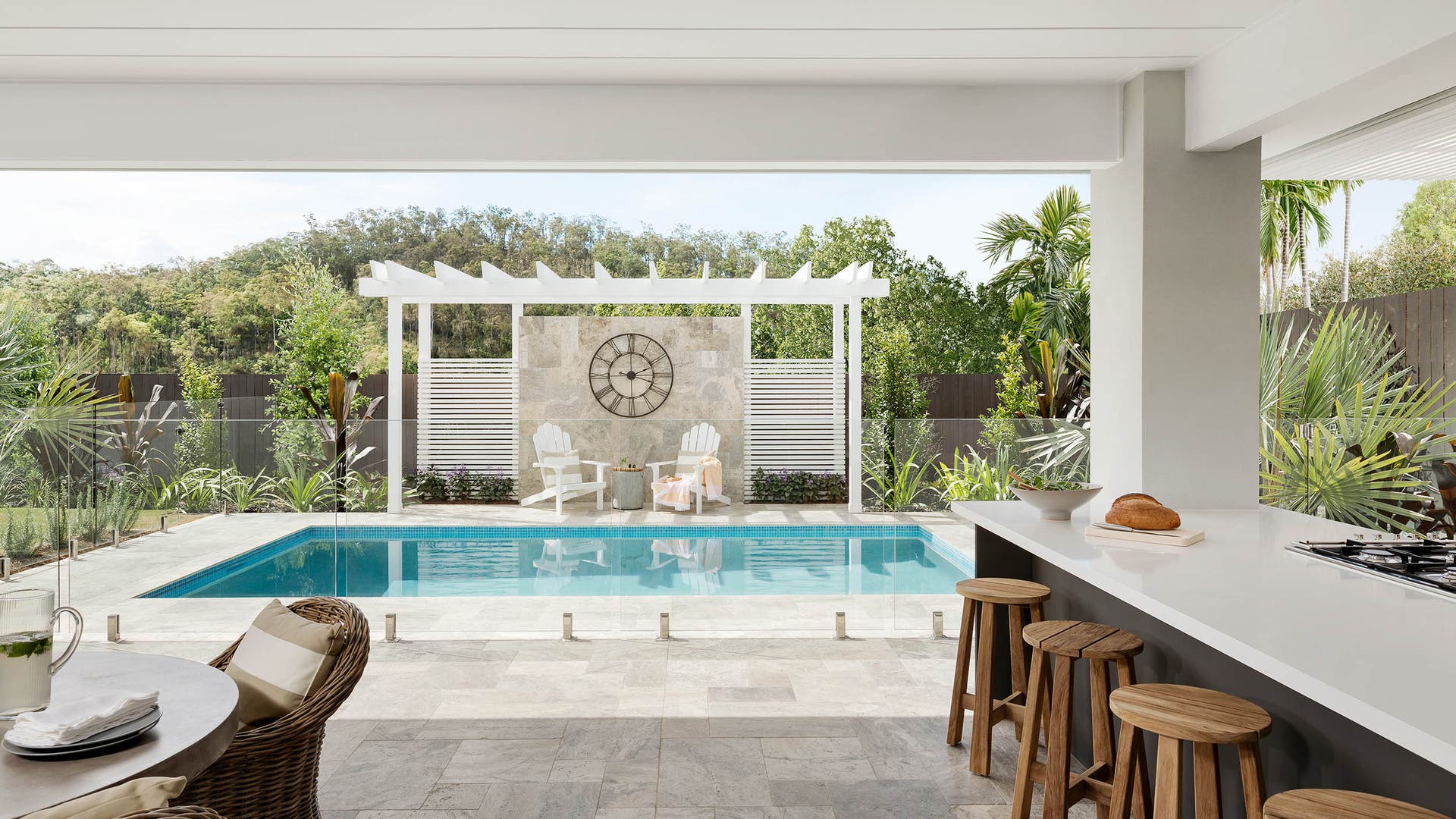 Alfresco and pool area with a glass divider, featuring a gazebo at the top of the pool and styled with a large round clock.