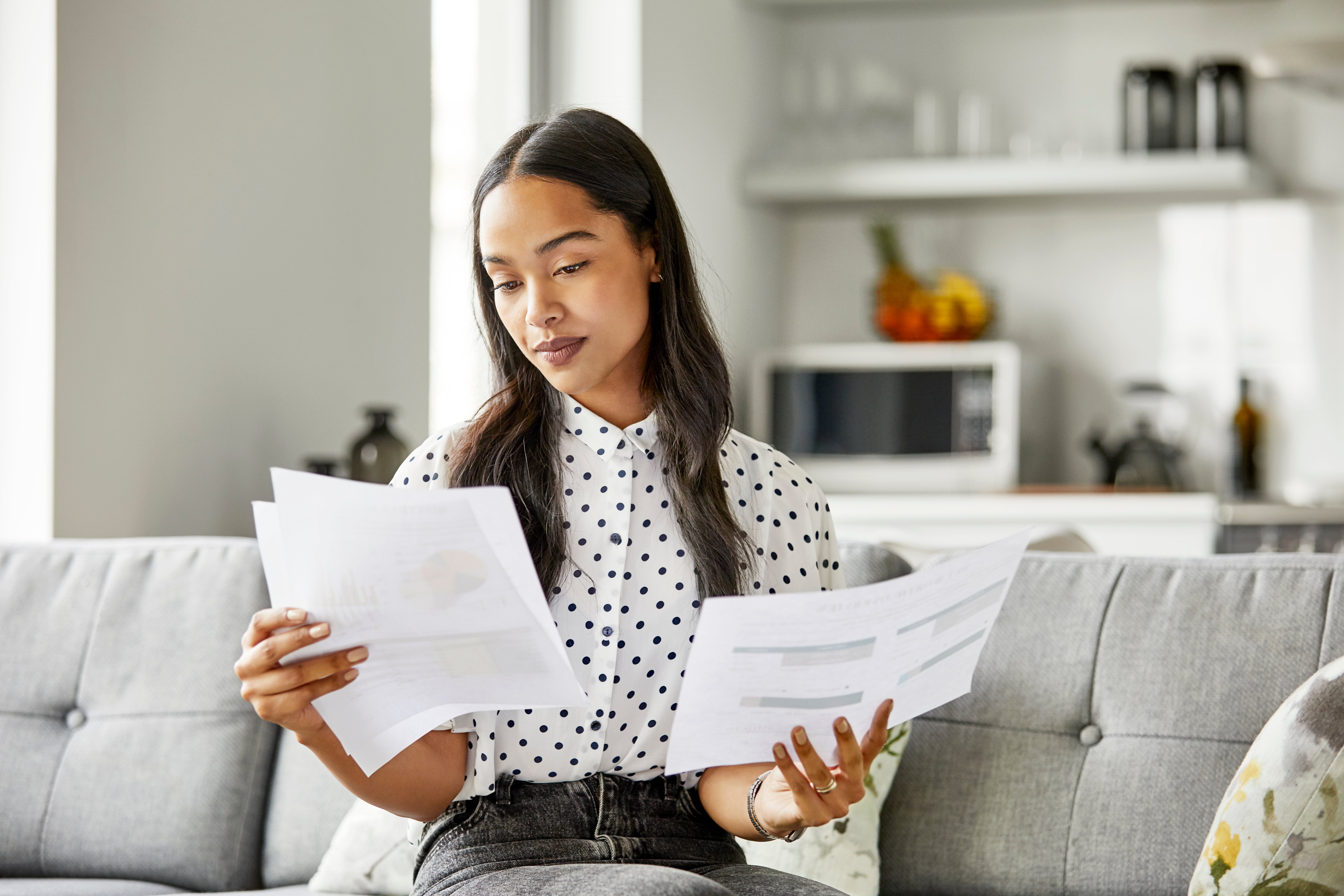 Young woman checking financial documents. Female is analyzing bills in living room. She is sitting on sofa at home.