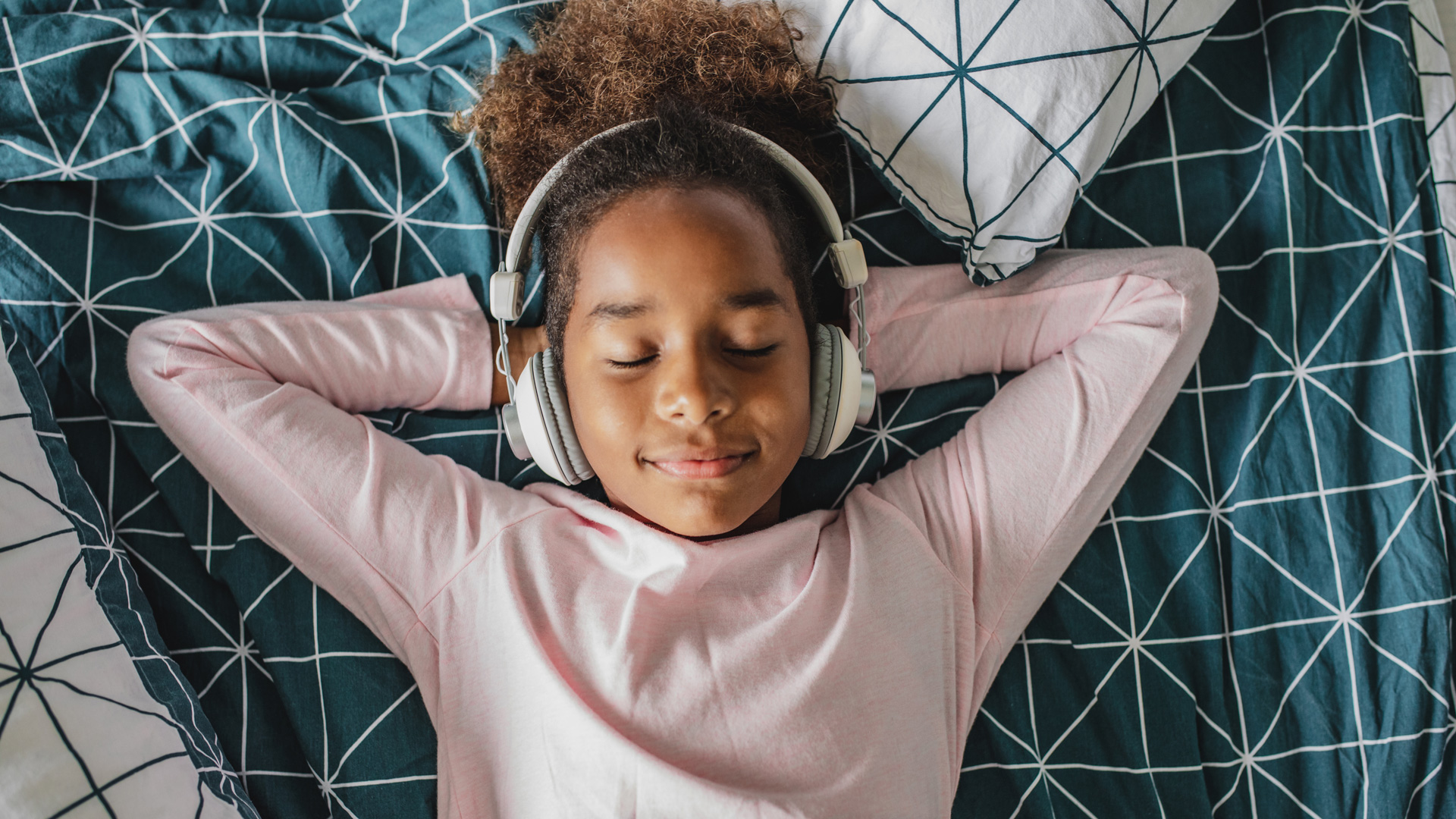 Smiling African American girl lying on bed while listening to headphones