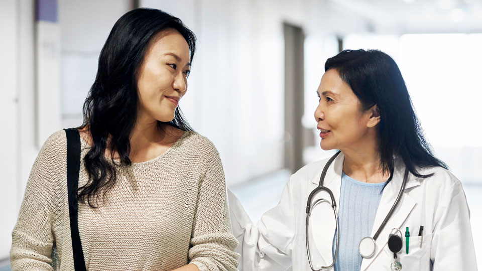 female doctor wearing a lab coat with a stethoscope around her neck walking next to female patient, talking 