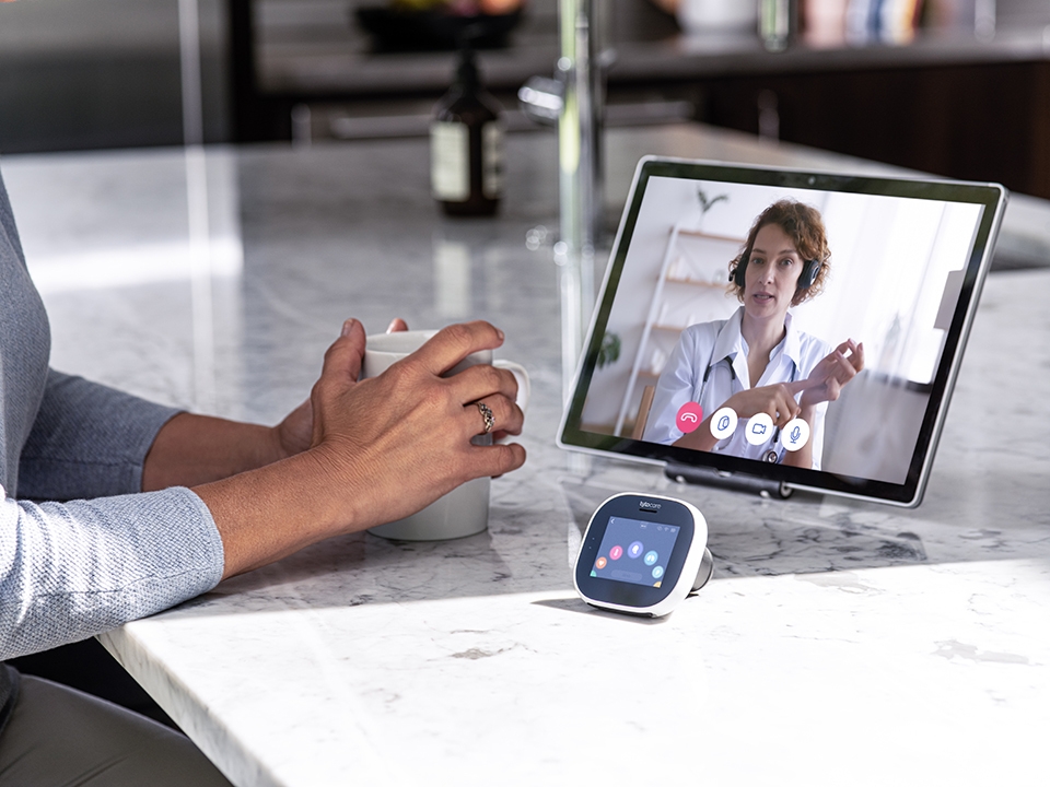 tytocare device sitting on a countertop in front of a tablet with a doctor on the screen speaking