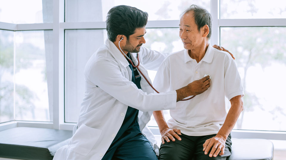 male physician in lab coat listening to male patient's chest with a stethoscope