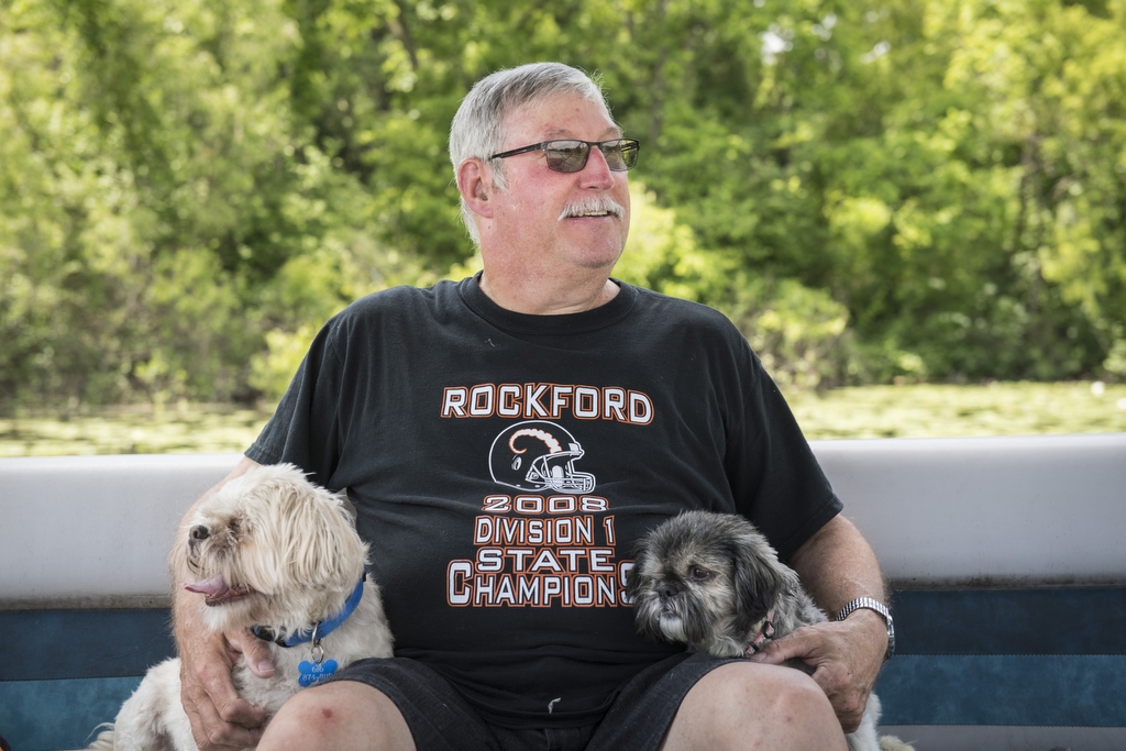 Older man wearing a black shirt shits with a small dog on each of his sides