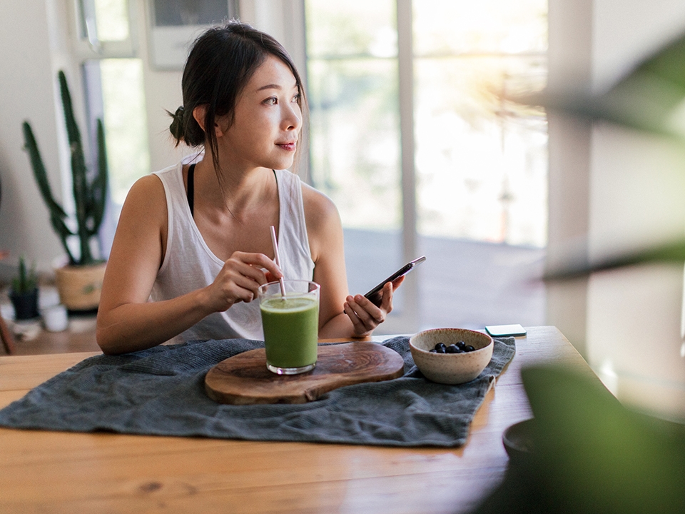 Woman drinking green beverage while holding cell phone.