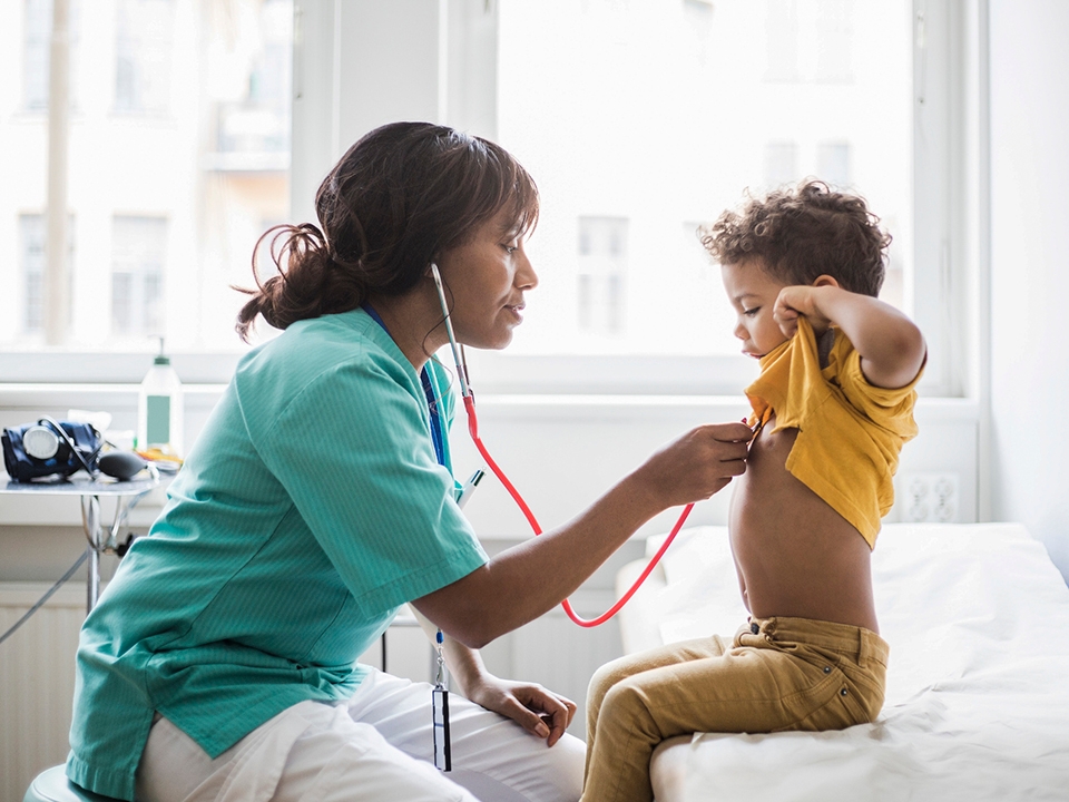 Healthcare provider using stethoscope on young boy's chest.