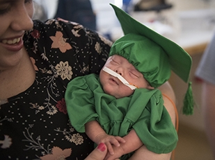 Preemie in a green graduation cap and gown