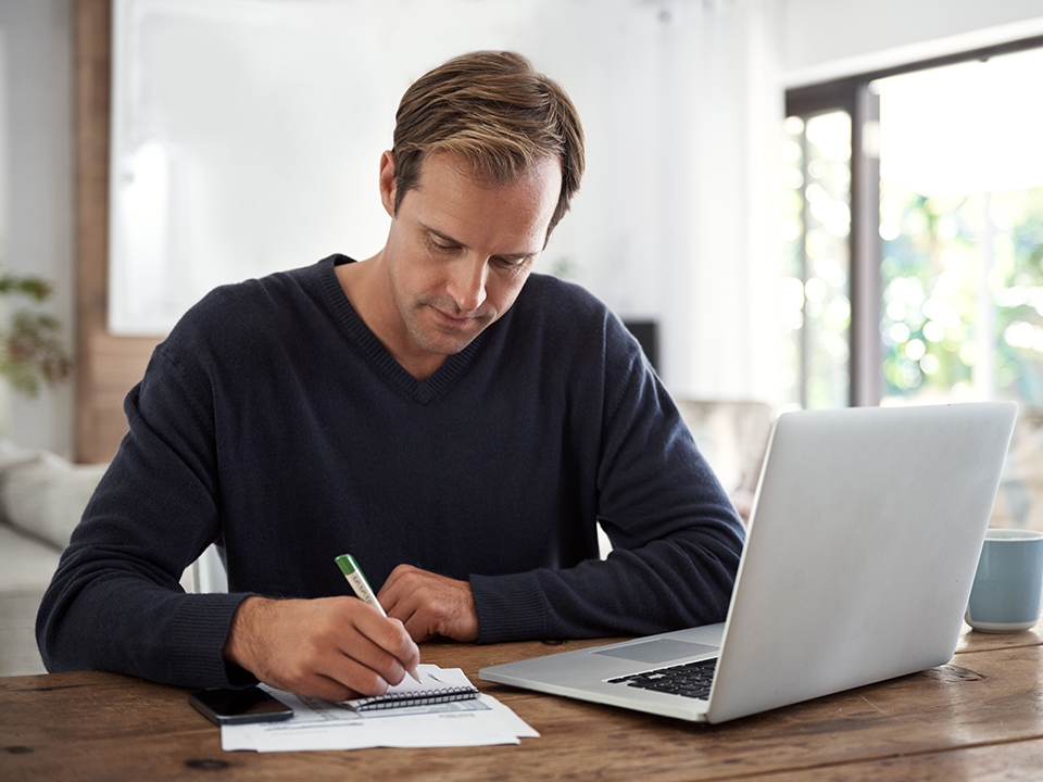 Man working on paperwork in front of laptop.