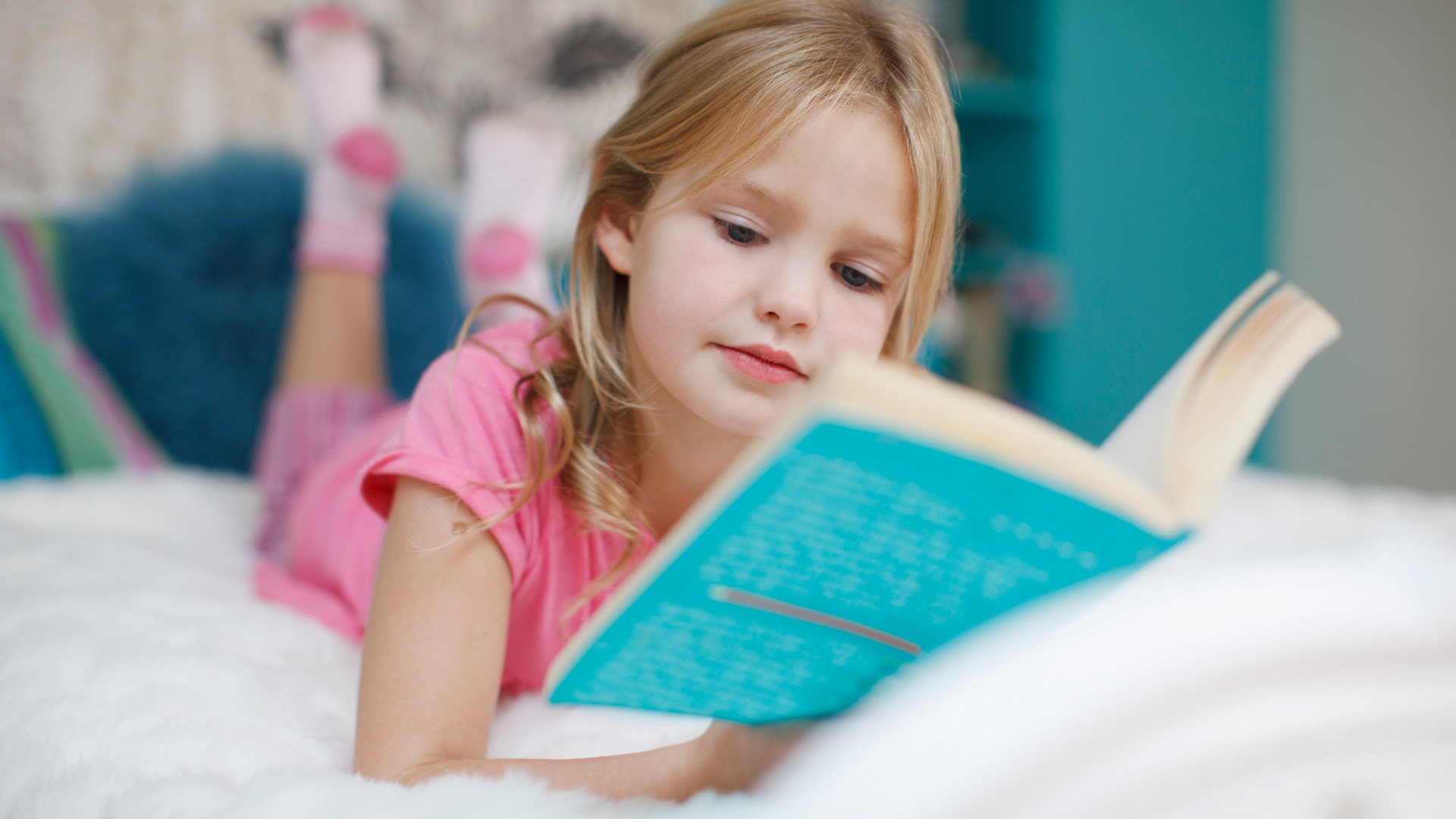 Young Caucasian girl in a pink shirt lying down and reading a book
