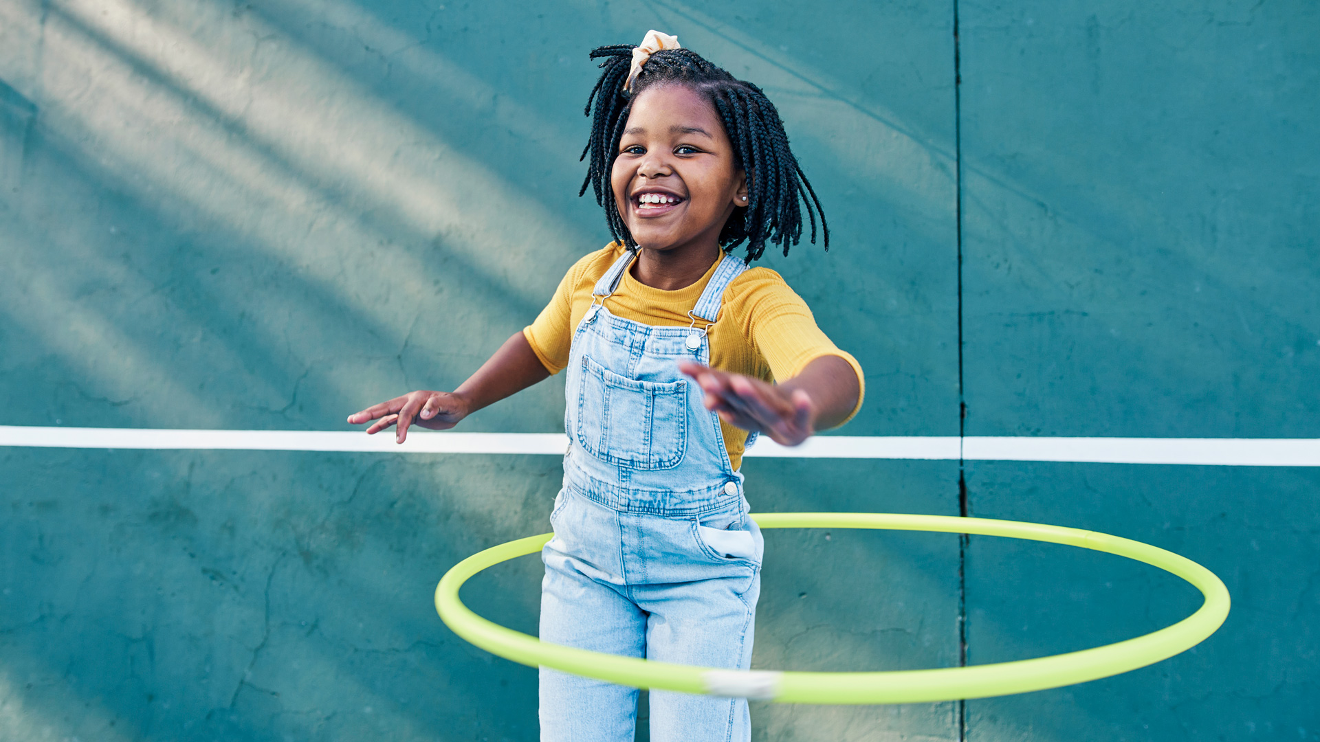 African American girl in denim overalls and yellow shirt playing with a hula hoop 