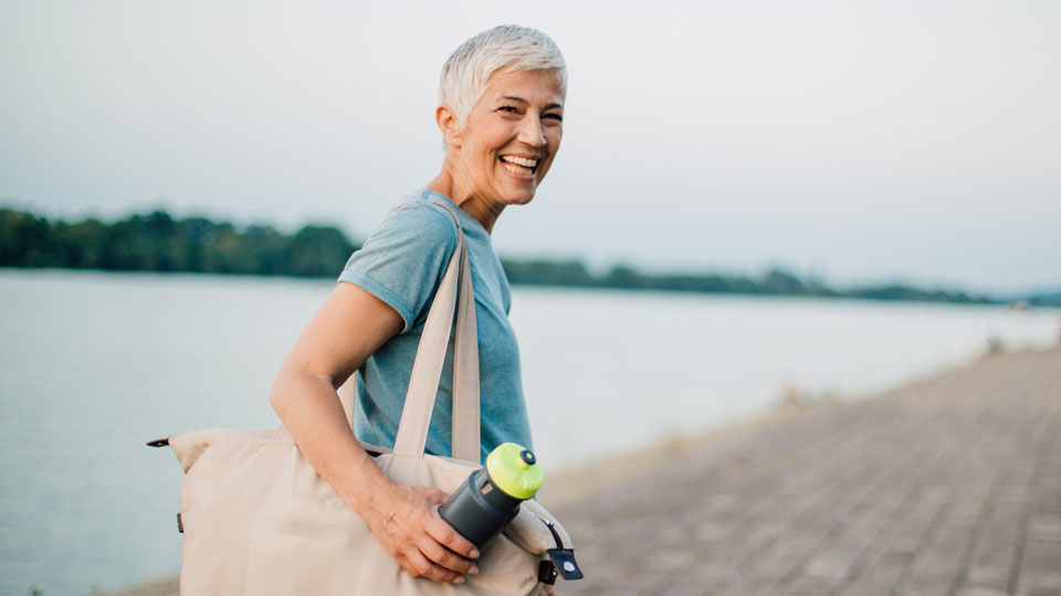 Active older woman with white hair smiling while walking near water