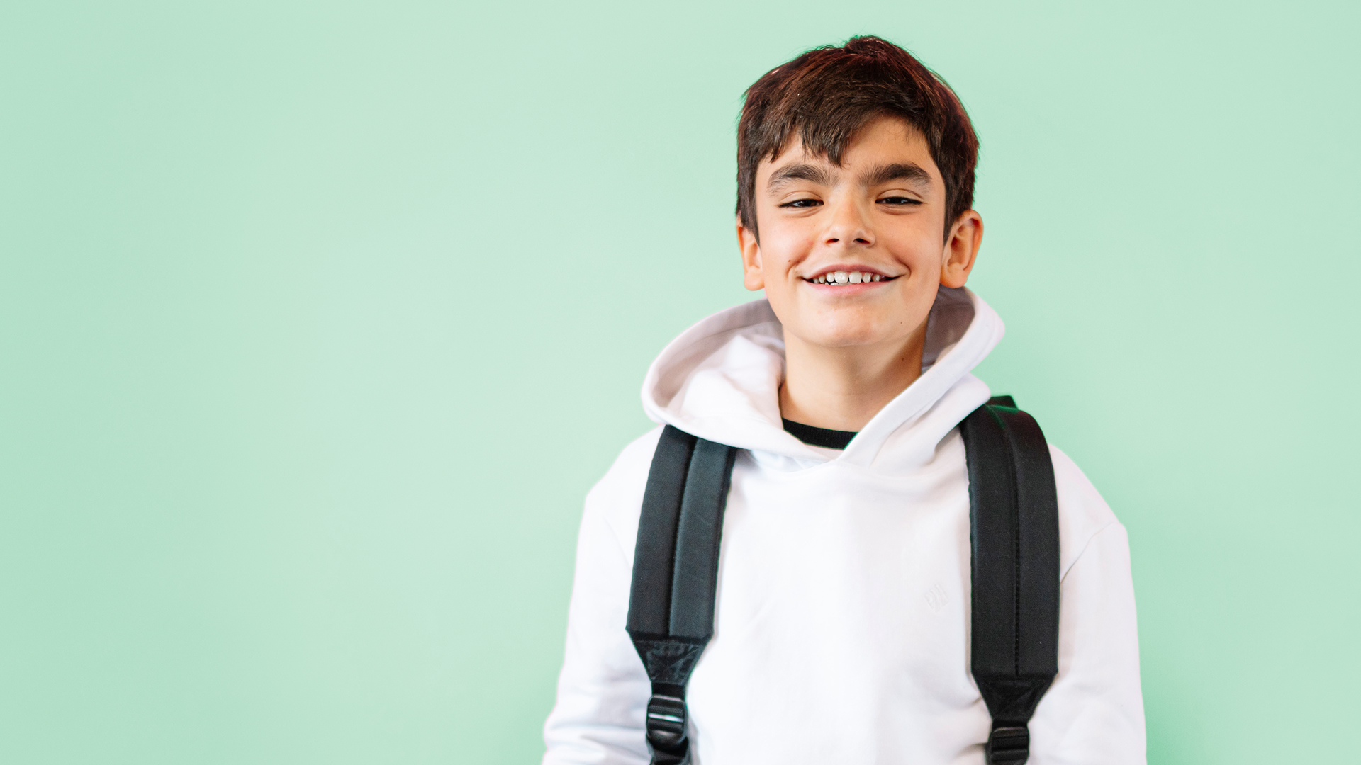 Smiling preteen boy in a white sweatshirt and wearing a backpack