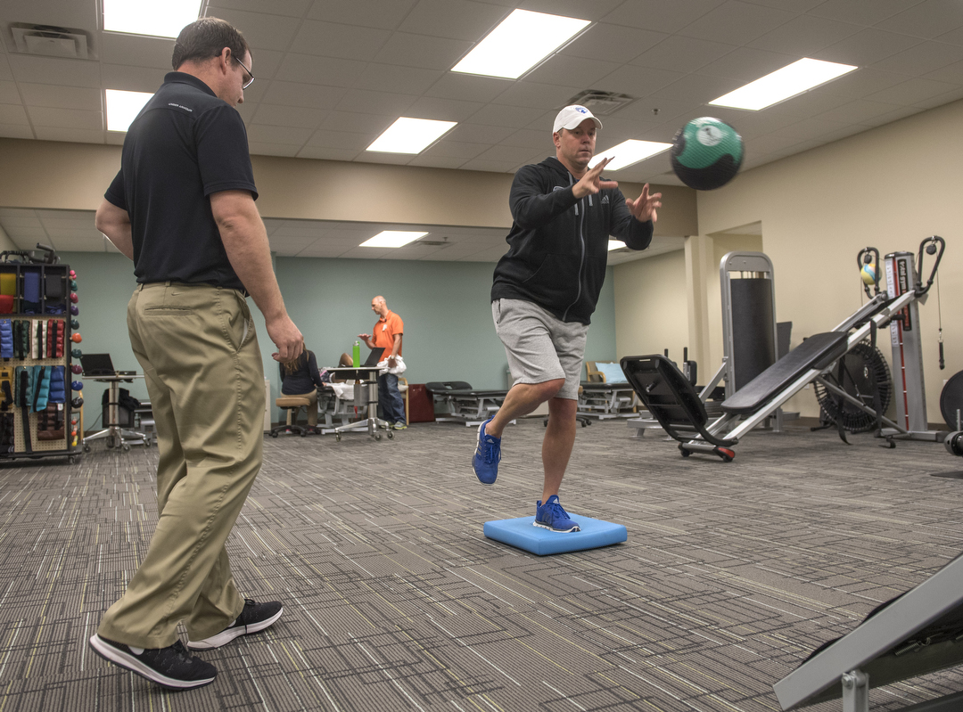 Trainer watching patient balance while throwing medicine ball