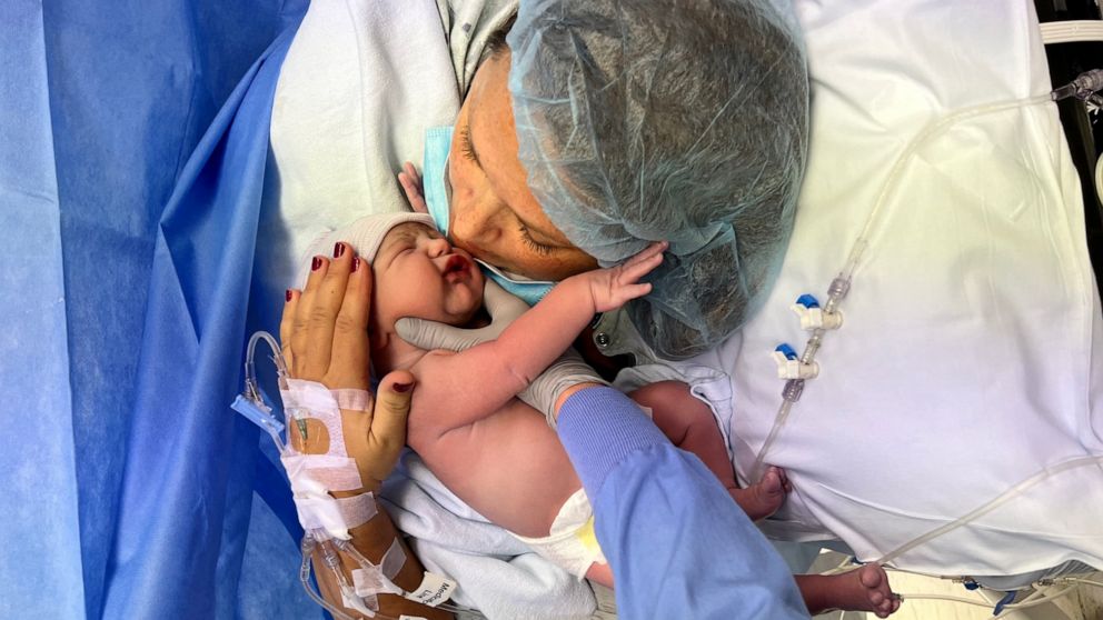 Woman in surgical gown kissing baby.