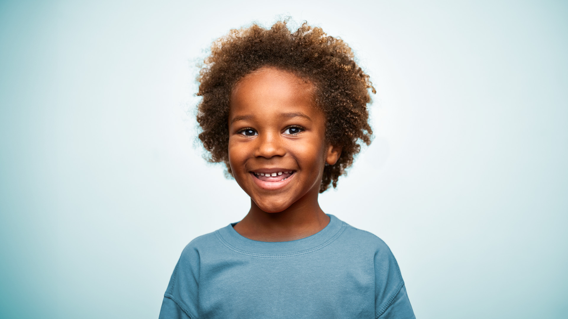 Smiling young African American boy with curly brown hair, in a blue shirt