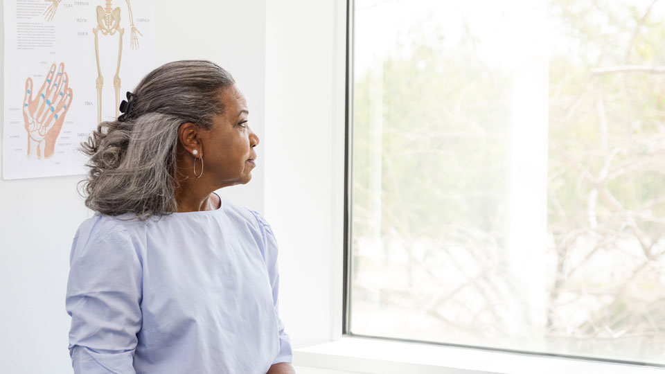 black woman with grey hair wearing exam gown sitting and looking to the side out a window