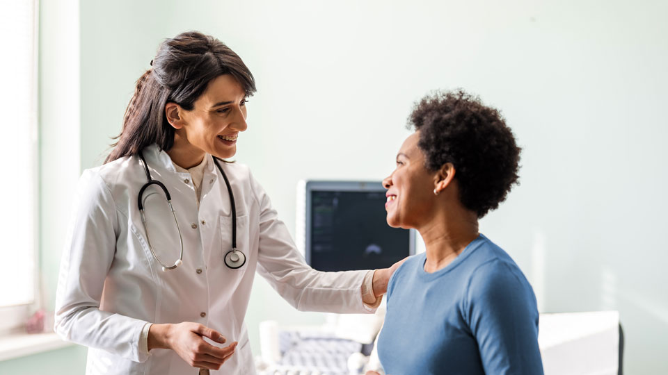 Female doctor standing next to female patient as both smile