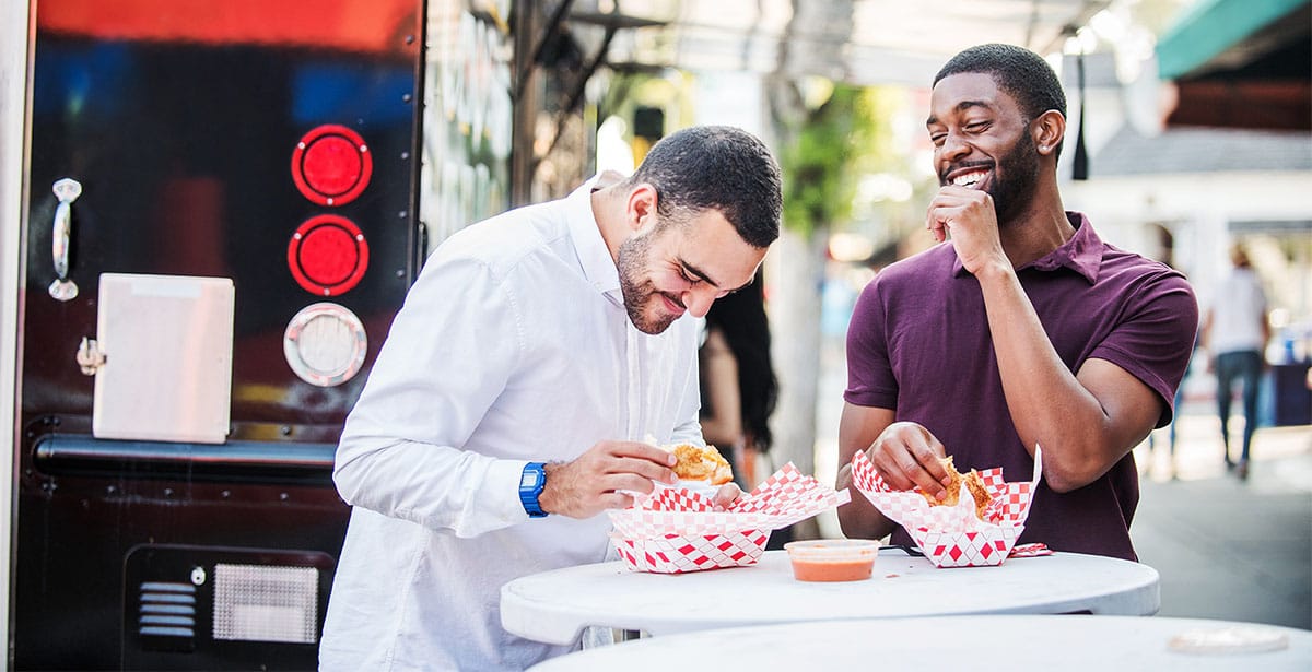 Two friends eating street food and laughing together