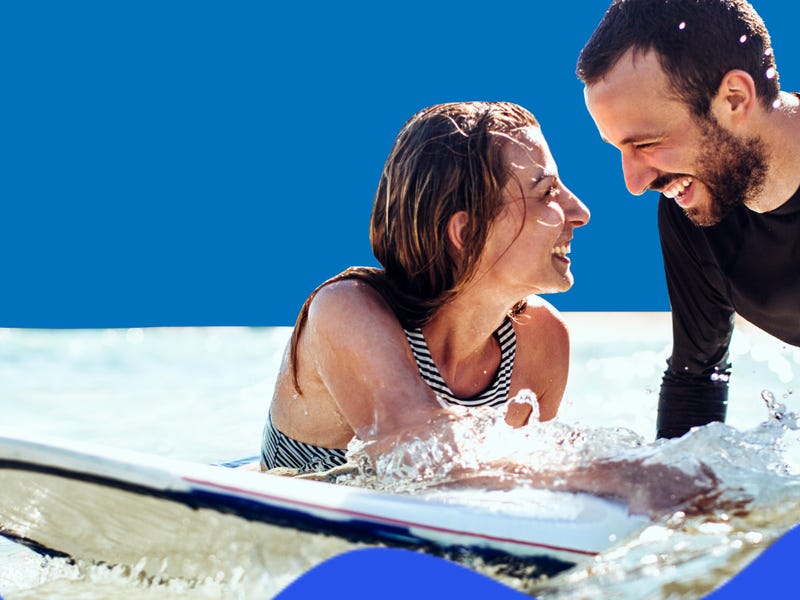Man and woman in the water with a surf board smiling at each other