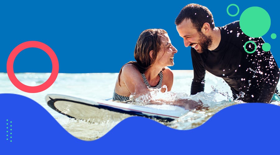 Man and woman in the water with a surf board smiling at each other
