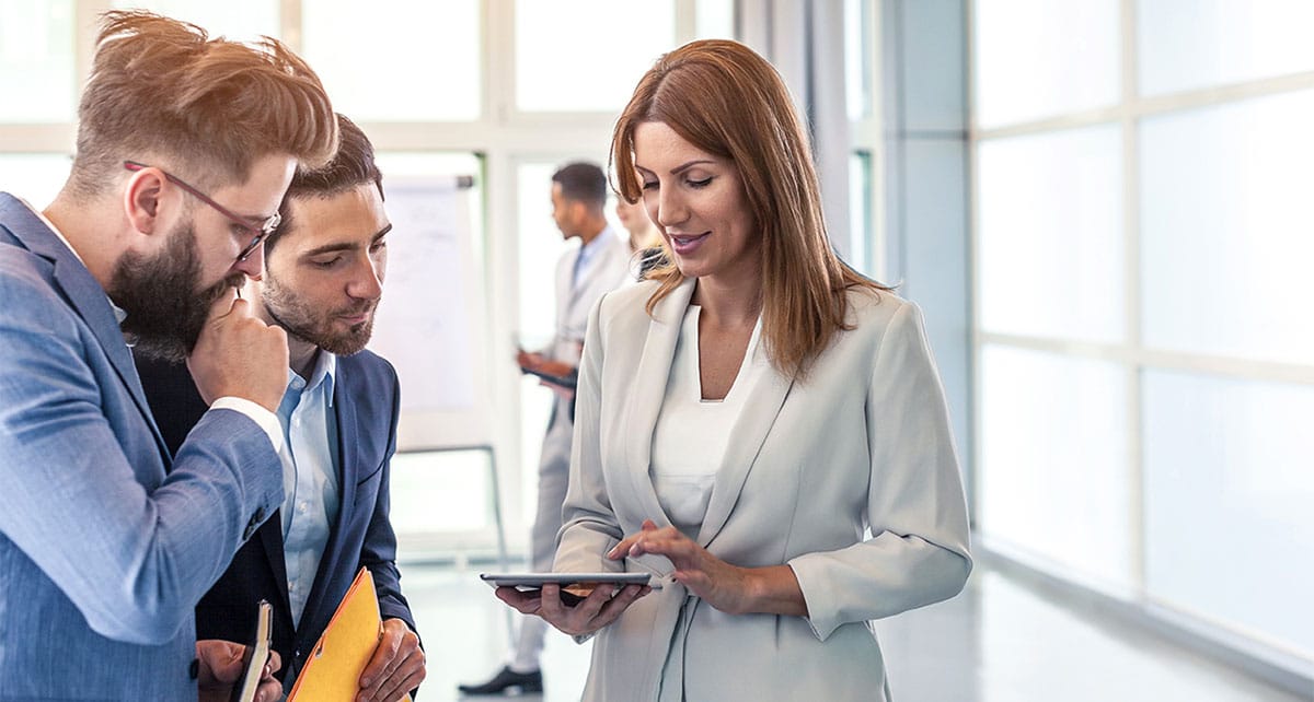Woman talking to people and showing them her contacts on a tablet while networking in a business meeting