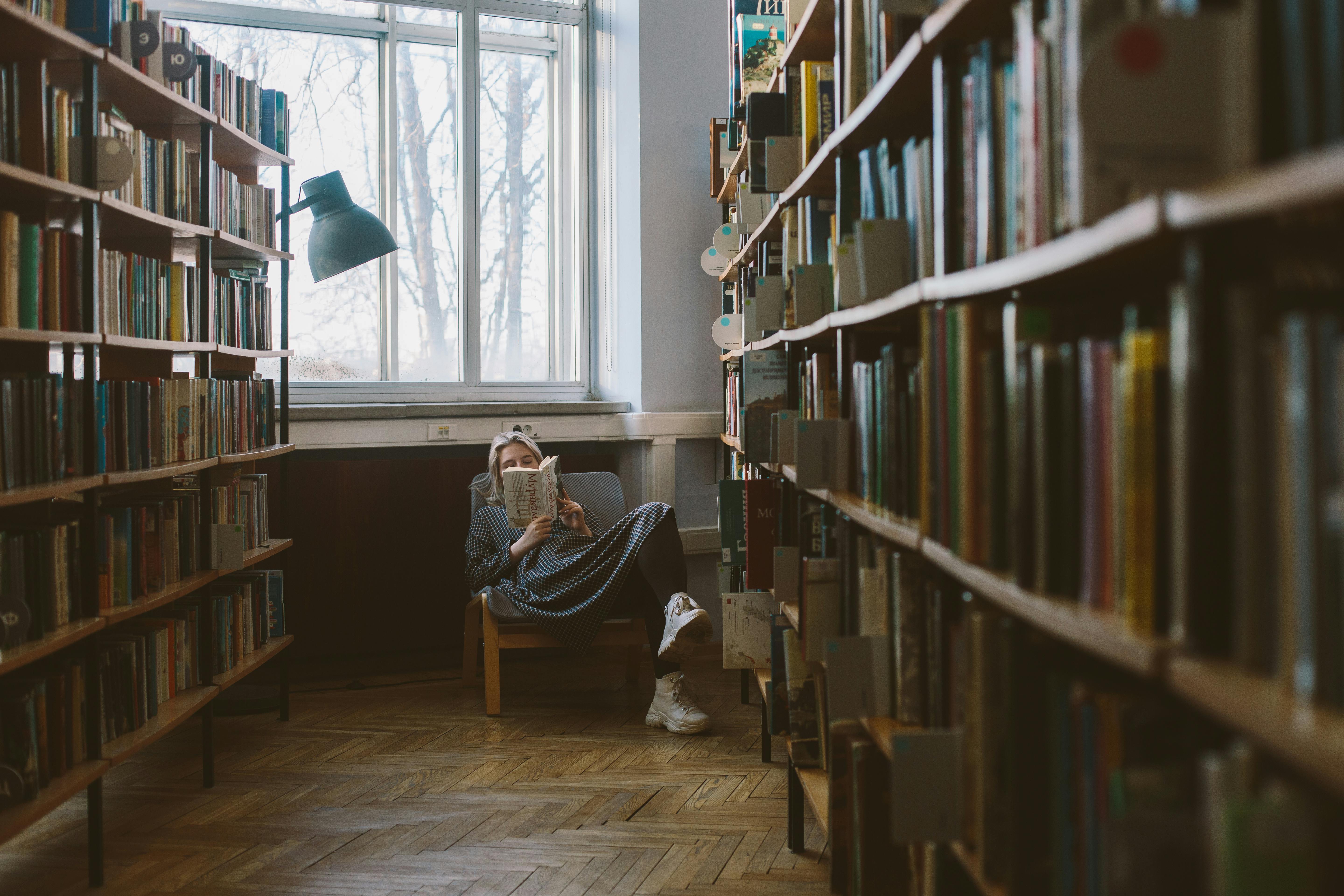 Woman in a fotel in a library reading a book