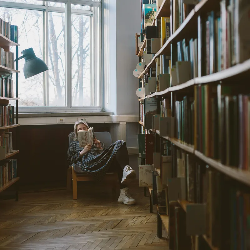 Woman in a fotel in a library reading a book