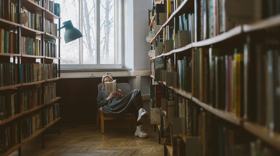 Woman in a fotel in a library reading a book