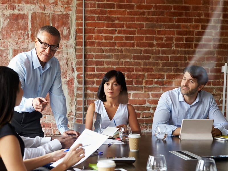 Group of professionals sitting at a table and listening to their language instructor during business language learning