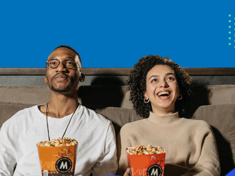 A couple sitting on a couch and eating popcorn while watching a movie