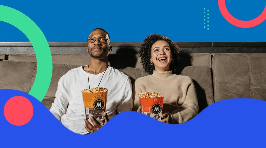 A couple sitting on a couch and eating popcorn while watching a movie