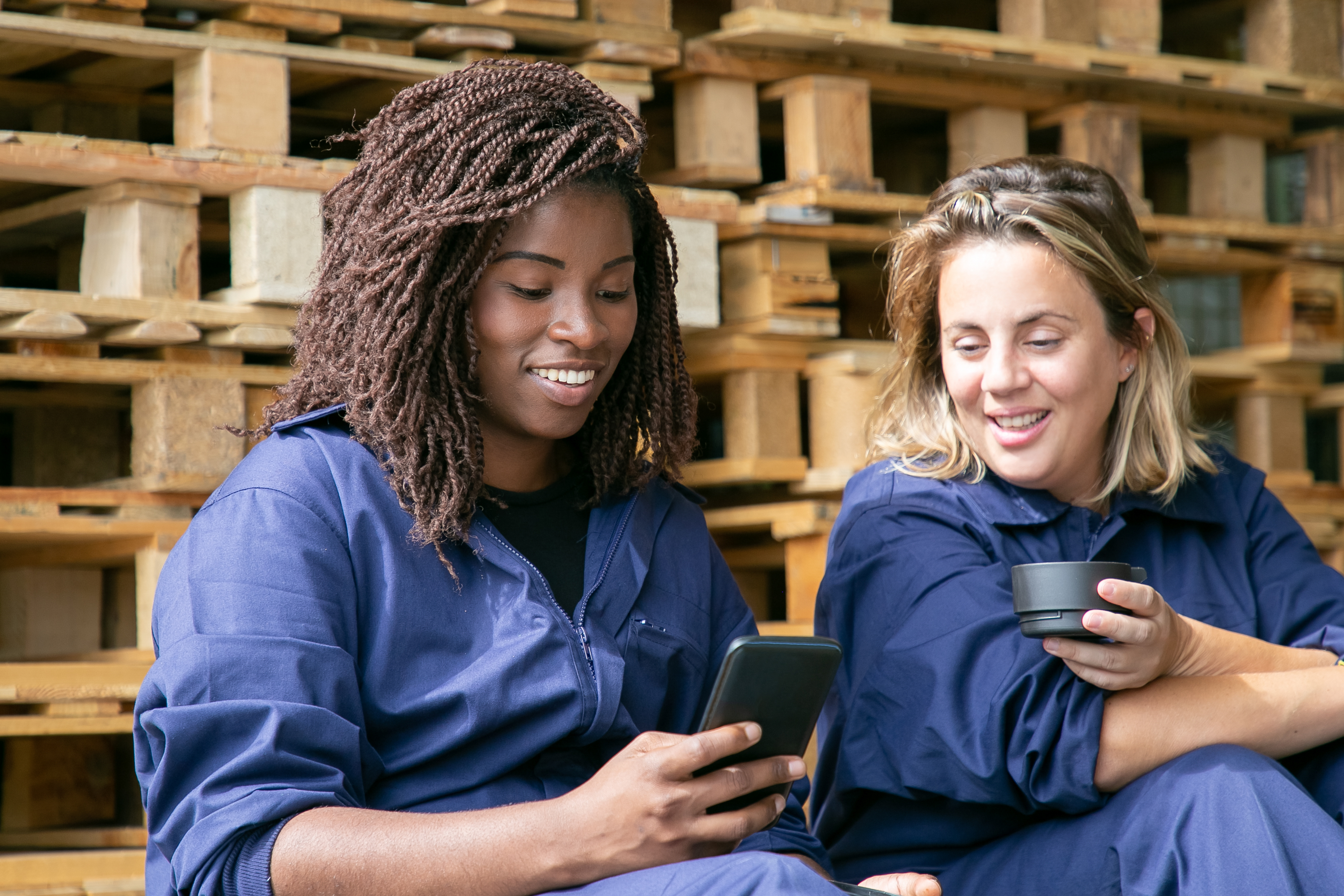 Two women at work looking at a phone, drinking coffee and chatting in English.